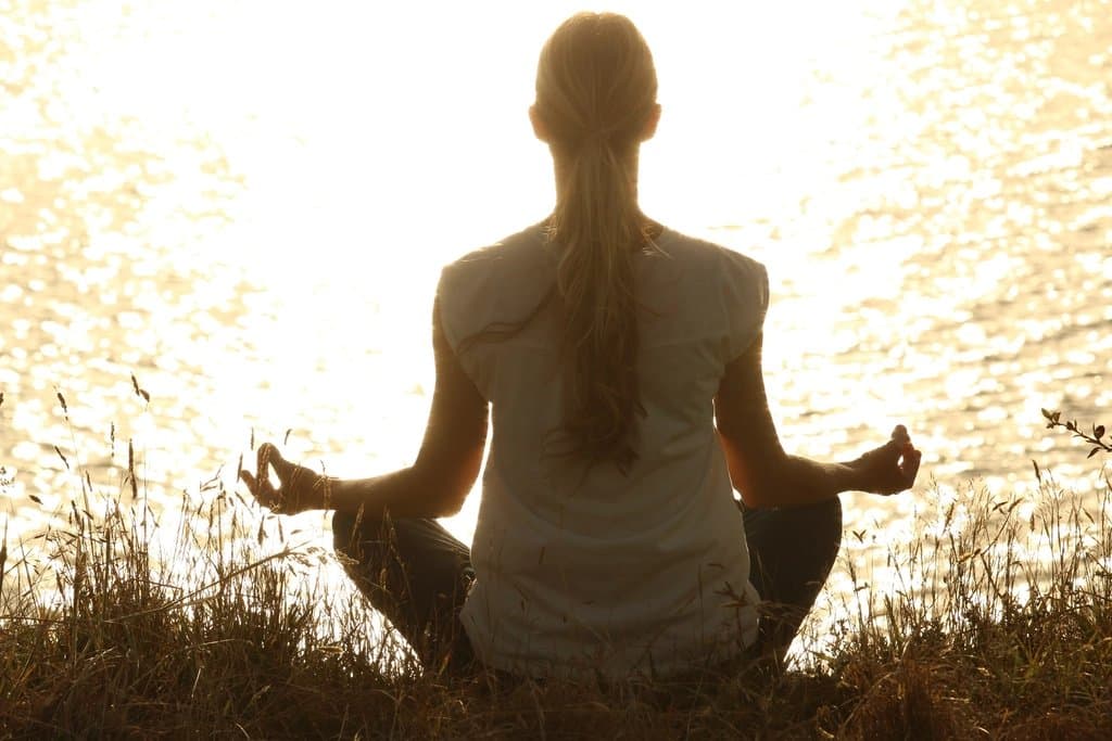Person sitzt bei Sonnenaufgang in Meditationshaltung